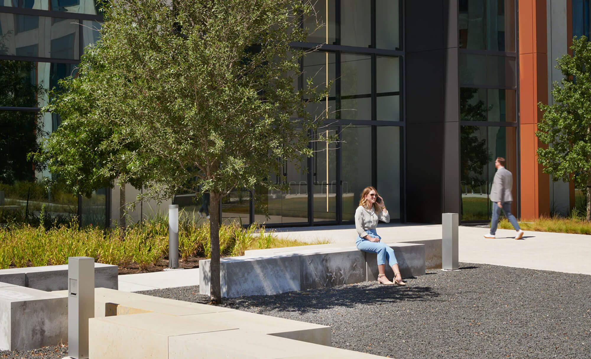 Woman sitting outside Parmer 5 building with modern glass architecture and plants