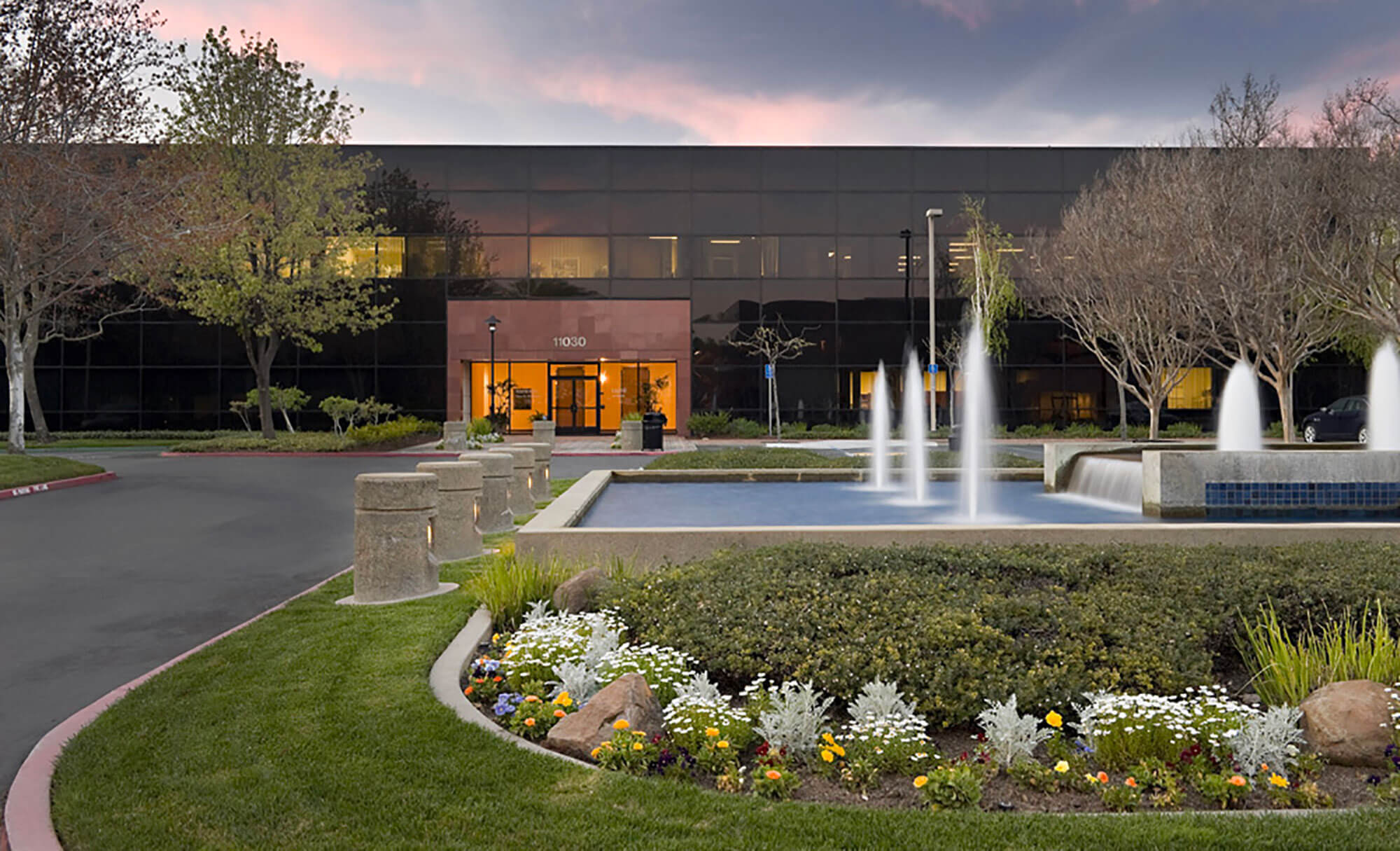 Evening view of Parmer West entrance with illuminated fountains and gardens