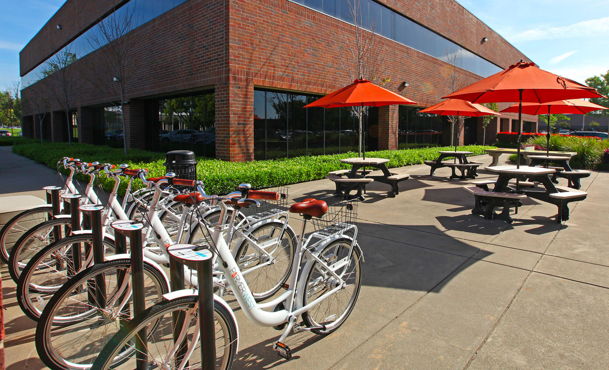 Outdoor bicycle rack and seating area with red umbrellas at Parmer West