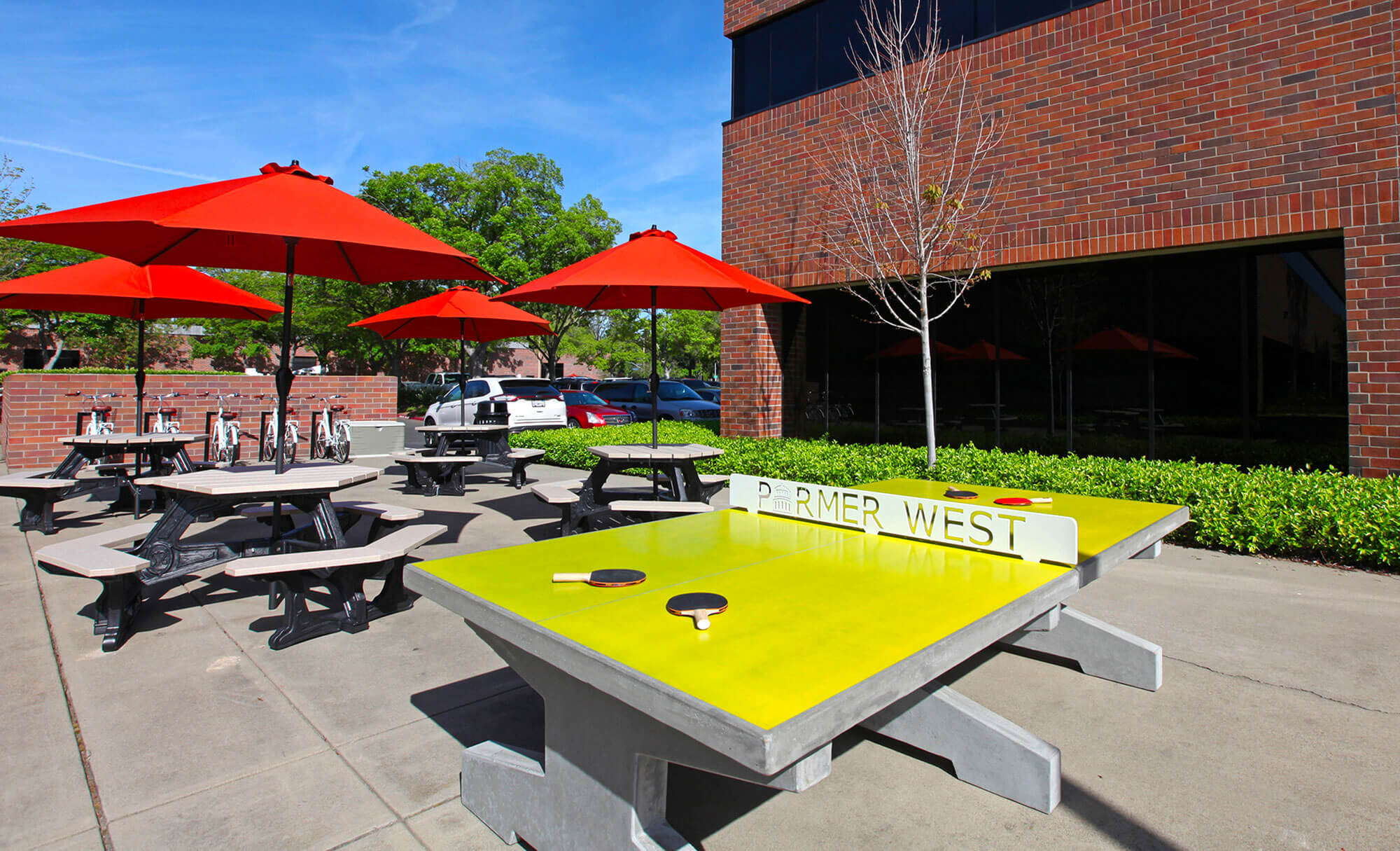 Parmer West courtyard featuring ping pong table and red umbrellas-shaded picnic areas