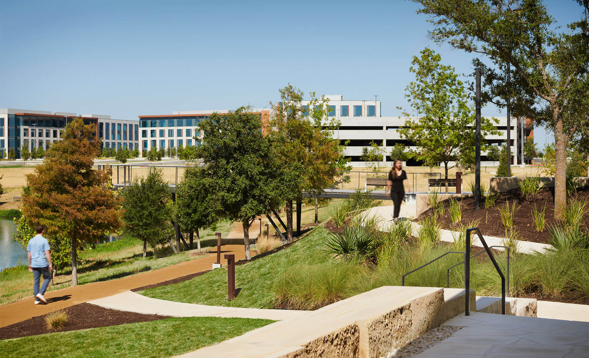 People walking along the scenic paths at The Pitch, with modern buildings and lush greenery
