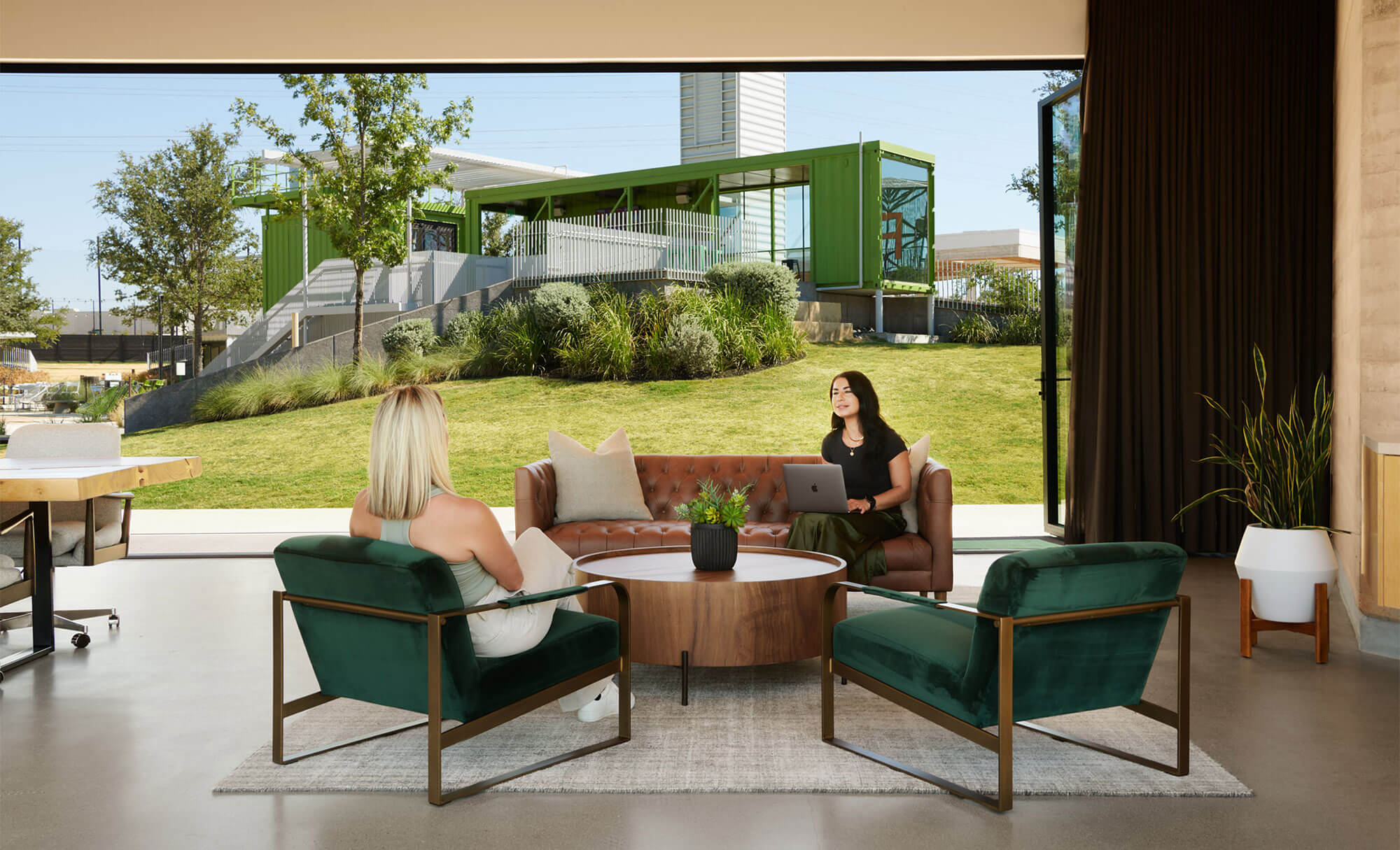 Indoor meeting space at The Pitch with two women discussing, overlooking lush outdoor area